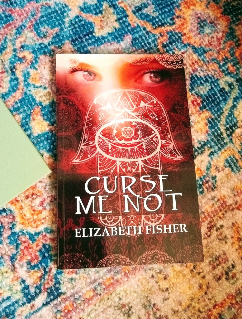 Closeup of Elizabeth Fisher's "Curse Me Not," with a woman's eyes gazing out over mystical symbols on the cover. 